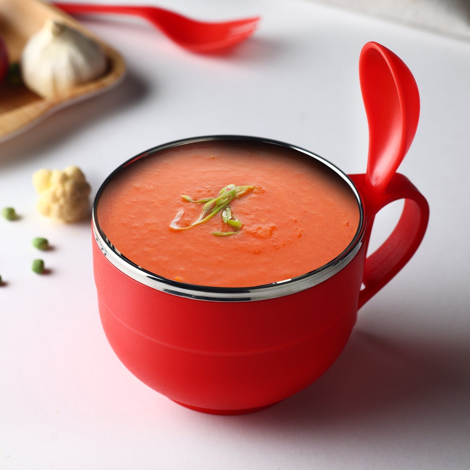 Stainless steel noodle bowl with spoon and lid on a vibrant background.
