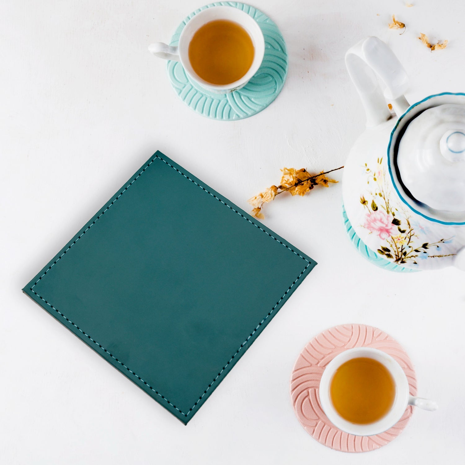 Square leather coaster protecting a wooden dining table from a cup.